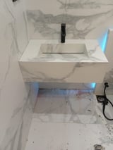 Modern white rectangular bathroom sink with black faucet mounted on marble-textured wall, LED lighting underneath, connected to plumbing