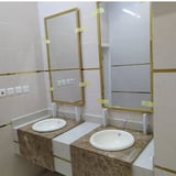 Modern bathroom vanity with two round white sinks, marble countertop, and brass-framed mirrors mounted on white tiled wall
