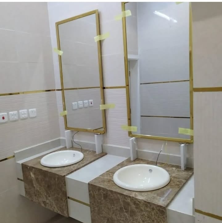 Modern bathroom vanity with two round white sinks, marble countertop, and brass-framed mirrors