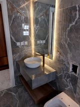Modern bathroom with dark marble walls, illuminated mirror, white vessel sink on floating vanity, and toilet below