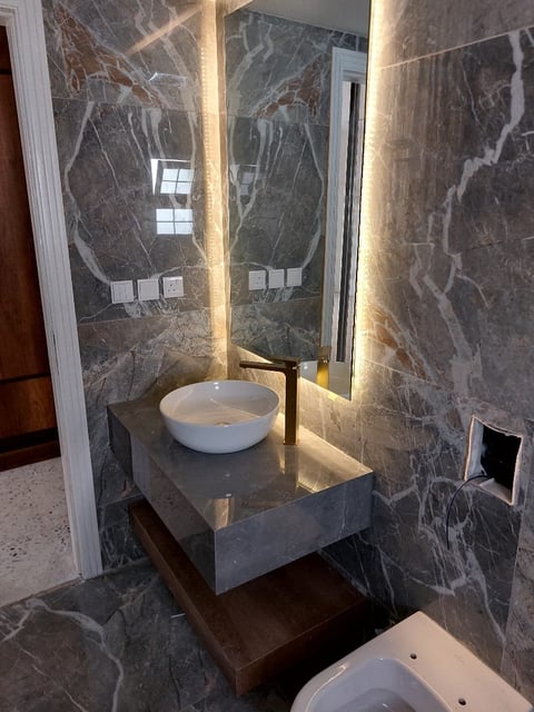 Modern bathroom with dark marble walls, illuminated mirror, white vessel sink on floating vanity