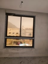 Interior window with black frame overlooking sandy buildings and streets during daytime