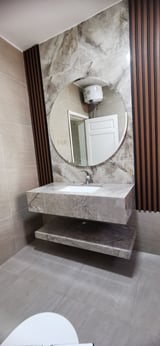 Modern bathroom with marble sink vanity, round mirror, wall-mounted heater, and brown vertical slat accent panels