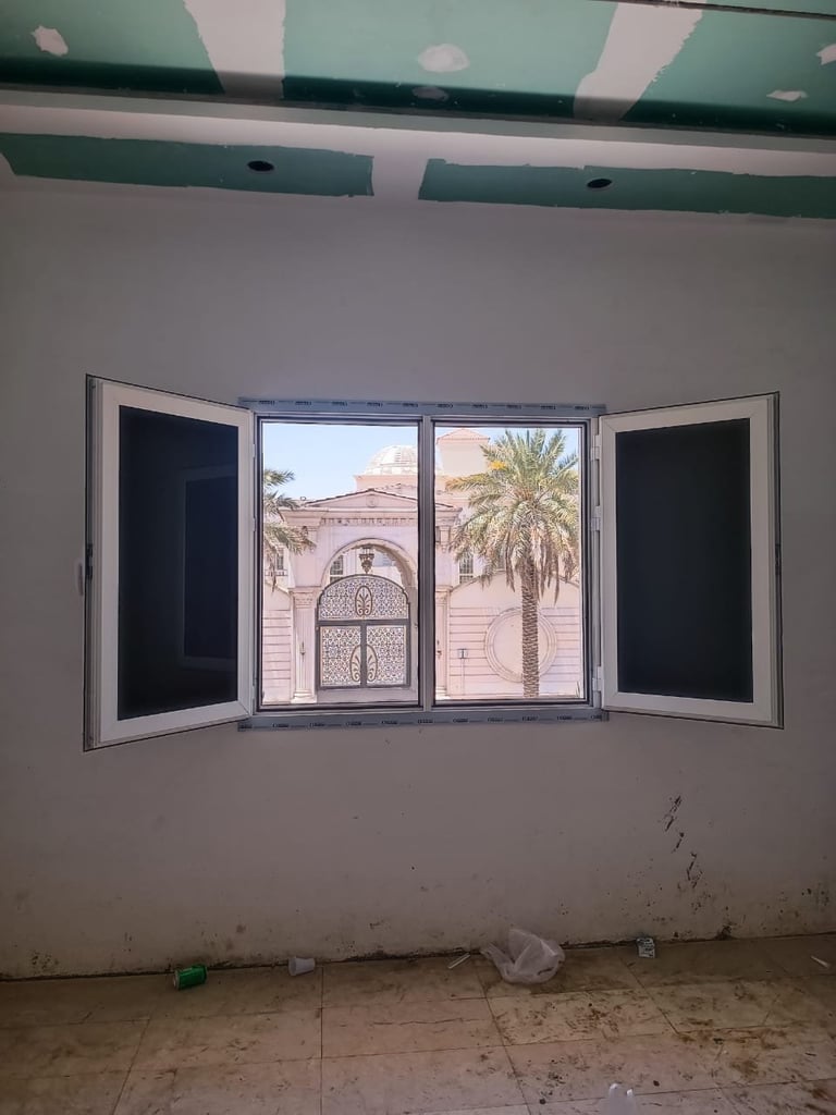 Four-panel window in under-construction room overlooking ornate building and palm tree through open panes
