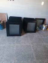 Stacked black window frames with glass panes leaning against white walls